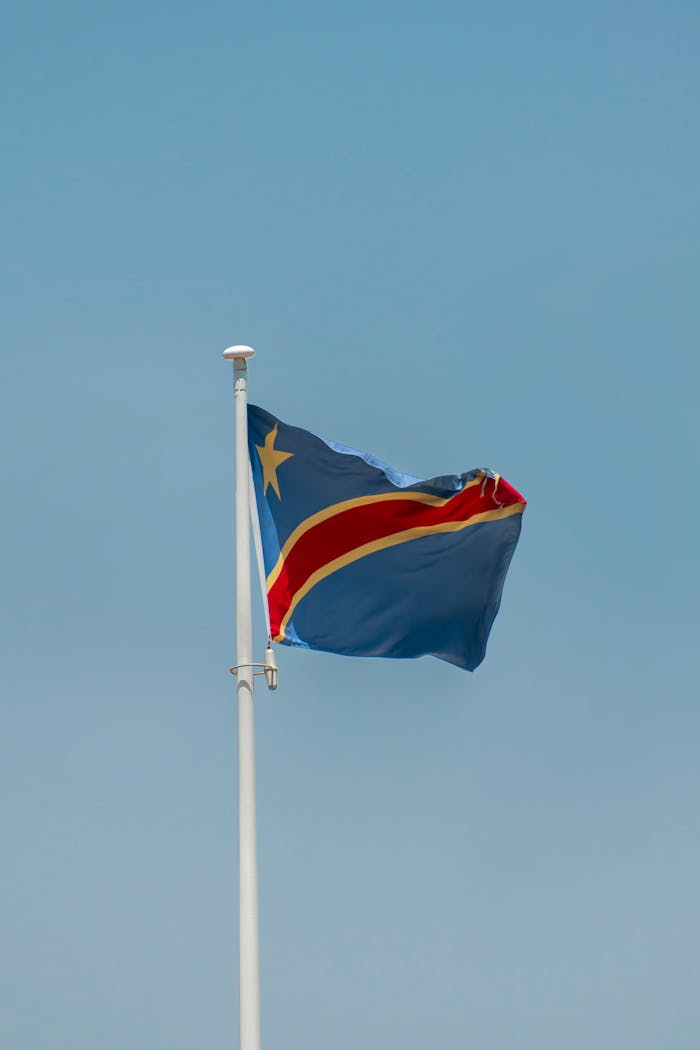 menu-01 Waving flag of the Democratic Republic of the Congo under a clear blue sky.