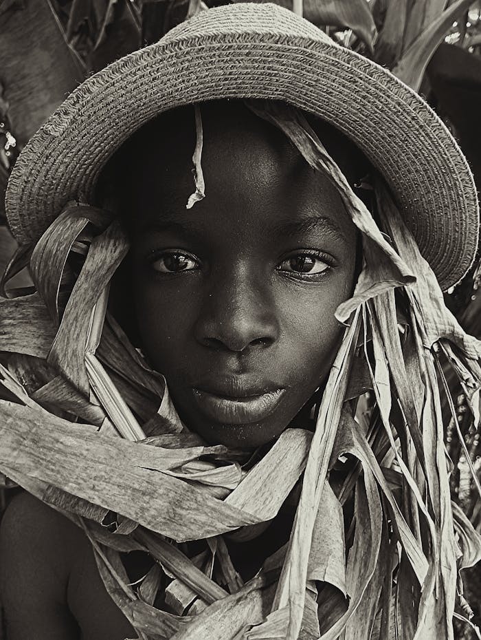 menu-08 Striking black and white portrait of a young boy wearing a sun hat and surrounded by leaves.