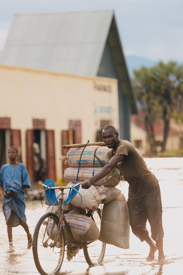 A man pushes a heavily loaded bicycle on a flooded street in a village during rain.